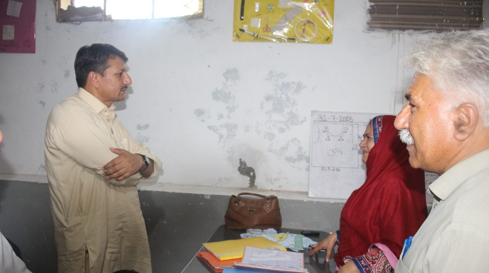 The District Social Welfare Officer in discussion with LEO staff beside a dated whiteboard at the skills centre