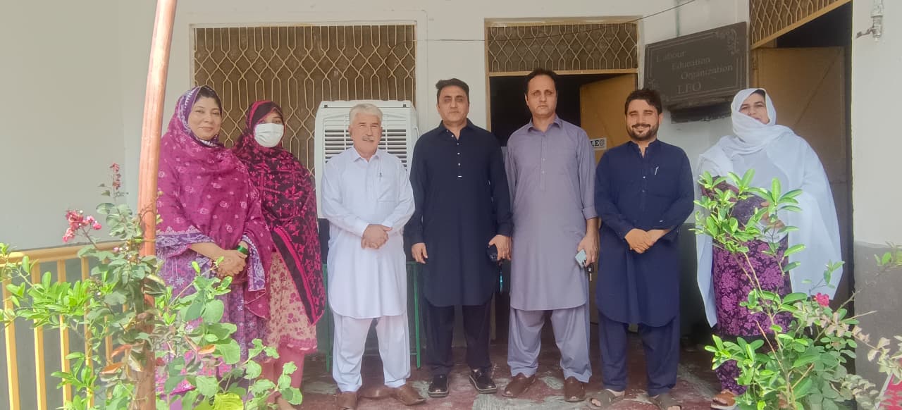 LEO board members and the programme team outside the organization's office in Mardan, with the signboard above the entrance