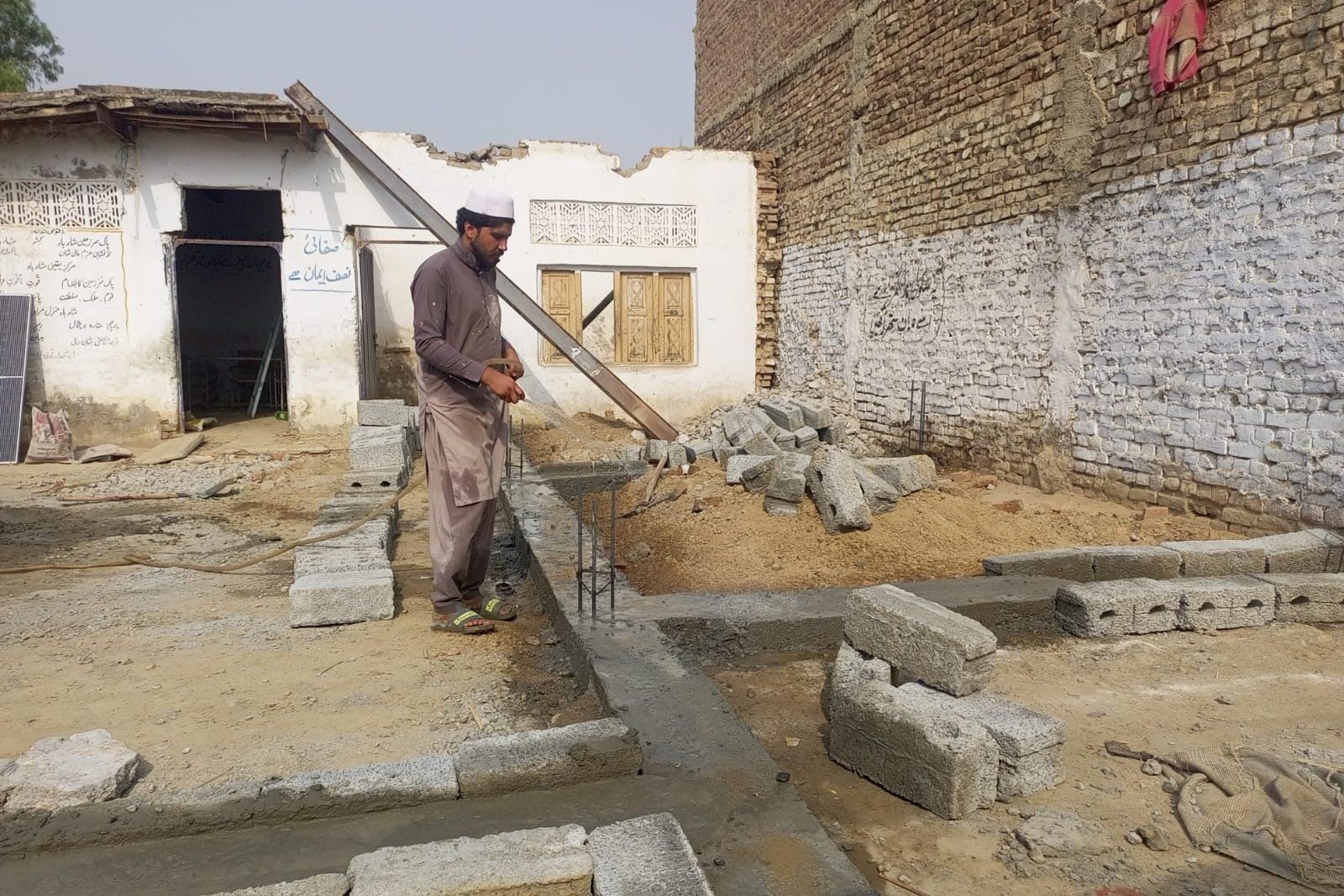 A worker hosing down fresh concrete in the foundation trench at the community school expansion site